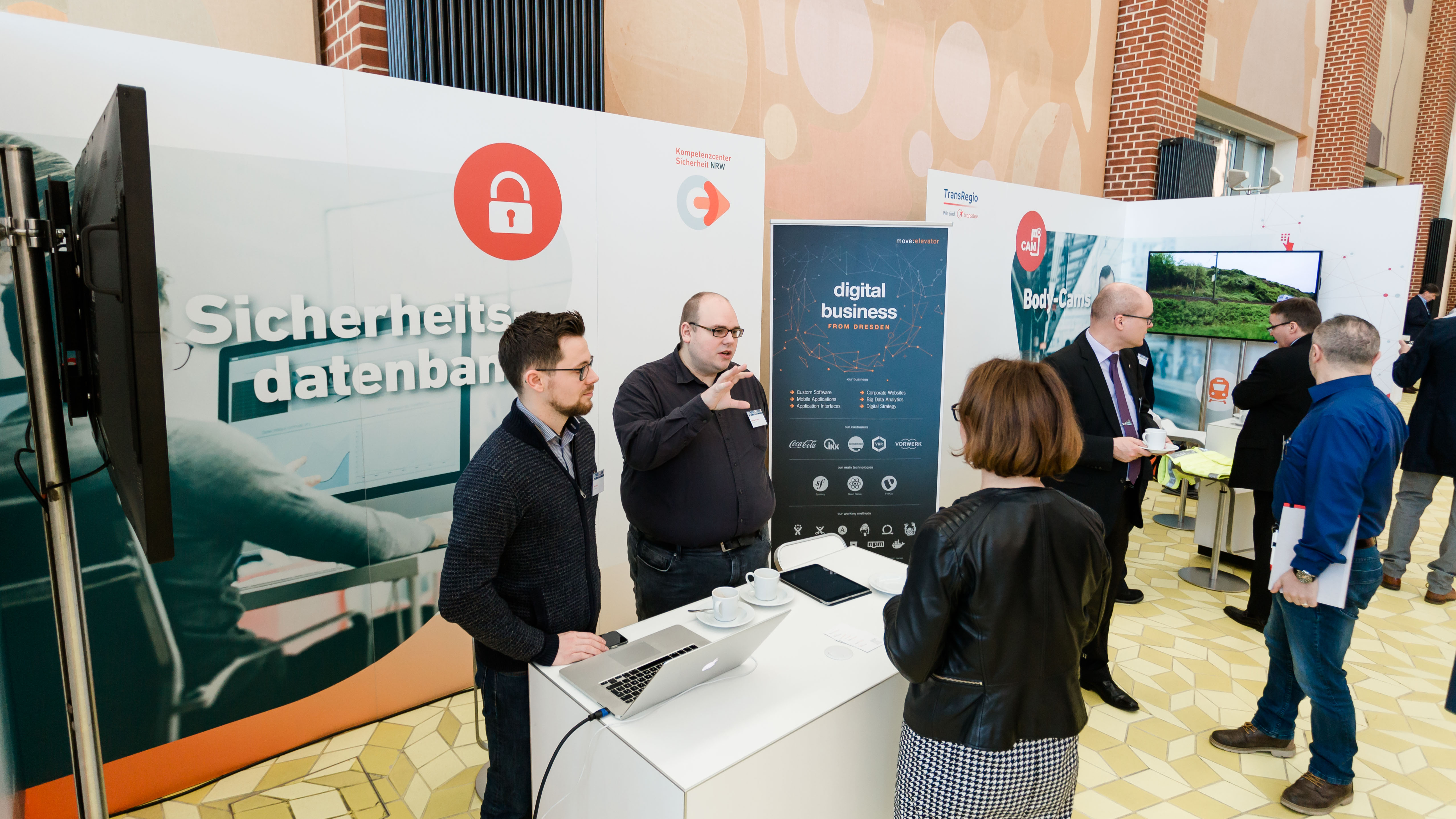 Zwei Aussteller zeigen einer Frau Informationen zur "Sicherheitsdatenbank". - öffnet Bild in größerer Ansicht